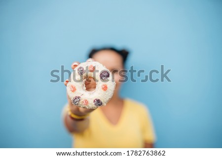 Happy portrait of a woman in yellow t-shirt eating donuts at blue wall