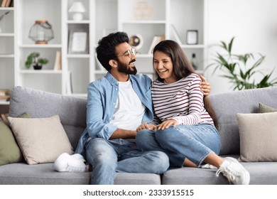 Happy positive beautiful loving young indian couple man and woman spending time together at home, sitting on couch in cozy living-room, embracing and laughing, lovers have conversation - Powered by Shutterstock