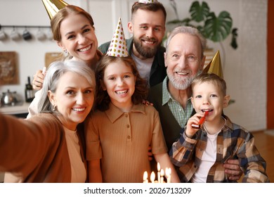 Happy positive big caucasian family grandparents, parents and two kids making selfie during birthday celebration at home, wearing party hats and smiling cheerfully at camera while standing indoors - Powered by Shutterstock