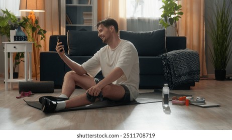 Happy positive Caucasian male man guy sportsman using mobile phone talking cellphone online call after hard sport workout showing thumb up holding towel trainer enjoying conversation indoor home room