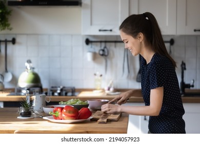 Happy positive chef blogger girl enjoying cooking, preparing salad for dinner, chopping fresh vegetables on board, using organic food ingredients, keeping healthy diet, lifestyle - Powered by Shutterstock