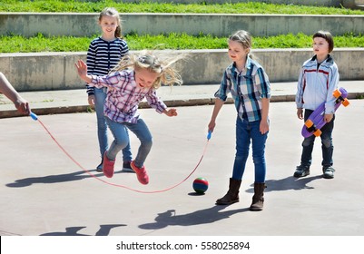 Happy positive children playing skipping rope jumping game and laughing outdoors