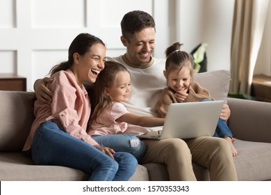 Happy Positive Family Young Parents Couple And Cute Little Children Daughters Laugh Using Laptop Computer Relax On Sofa Enjoy Watching Funny Videos Bonding Look At Notebook Screen Sit On Sofa At Home