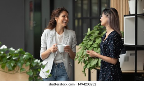 Felices y positivas colegas bromeando riéndose durante la pausa del café en el espacio de trabajo, sonriendo a diversas mujeres equipo de negocios hablando divirtiéndose disfrutando de la conversación buenas relaciones amistosas caminando en el cargo