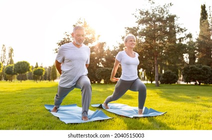 Happy Positive Fit Mature Couple Of Senior Woman And Man Practicing Partner Yoga On Open Fresh Air Outside Standing Barefoot In Warrior Virabhadrasana Pose In Nature On Open Air Of City Park Exterior