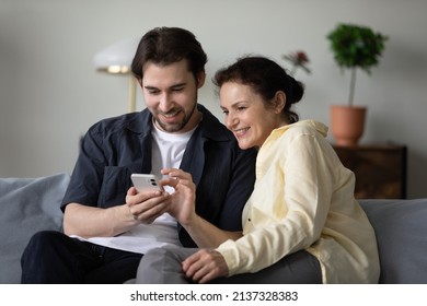 Happy positive grown son and mature mom using online virtual app, banking service on mobile phone, shopping on Internet together, making video call. Middle aged mother and grown child using gadget - Shutterstock ID 2137328383