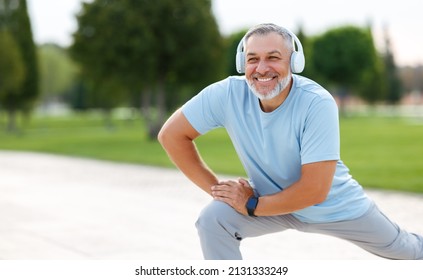 Happy positive mature sportsman during outdoor workout, senior man wearing headphones and sports outfit warming up muscles, doing side squat on one leg, enjoying active lifestyle outside in park