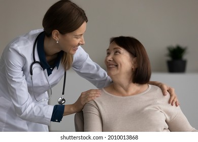 Happy positive medical professional, doctor, nurse giving support and help to senior female patient at appointment, touching shoulders. Old woman visiting, consulting young physician in office - Shutterstock ID 2010013868