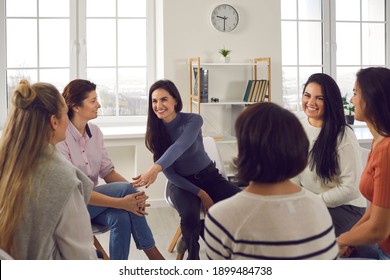 Happy Positive Smiling Female Coach, Therapist Or Business Team Manager Supporting And Motivating Young Women In Group Therapy Session Or Corporate Staff Training Meeting At Work