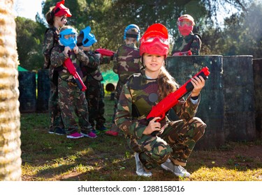 Happy Positive Smiling Teen Girl Wearing Uniform And Holding Gun Ready For Playing With Friends On Paintball Outdoor