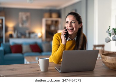 Happy positive woman entrepreneur sitting in home office, working on laptop computer, talking on cell phone. - Powered by Shutterstock