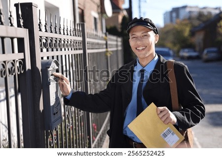 Happy postman putting envelope into mail box outdoors