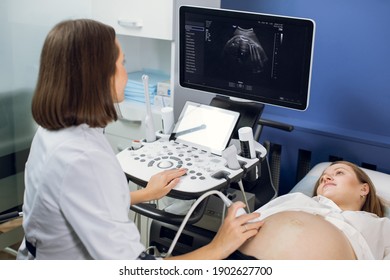 Happy Pregnancy Time, Ultrasound Concept. Pretty Pregnant Woman Doing Ultrasound Scan In The Prenatal Clinic, Worried About Health Of Her Future Baby. Female Doctor Looking At The Screen