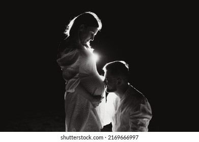 Happy Pregnant Couple. Mother And Father Love Expecting Baby During Pregnancy. Family Waiting Child Birth Over Black Night Background.