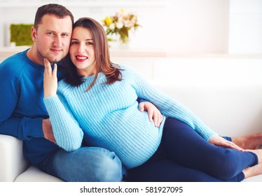 happy pregnant couple relaxing on couch at home