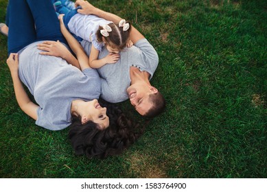 Happy pregnant family with little girl laying on grass and having fun in summer nature - Powered by Shutterstock