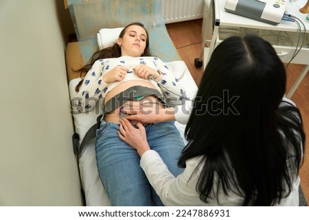 Happy pregnant female visiting her own gynecologist in medical clinic.Doctor examining the baby with stethoscope and ctg graph. Fetal heart monitoring. Cardiotocography.                             