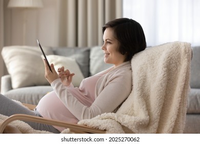 Happy Pregnant Girl Reading Book On Tablet Computer At Home, Using Virtual App, Shopping On Internet Stores, Buying Baby Clothes, Consulting Doctor On Online Chat. Expecting Mom Wit Digital Device