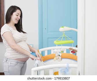 Happy pregnant mother equipping baby's cot in blue room, smiling. - Powered by Shutterstock