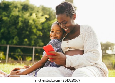 Happy Pregnant Mother And Son Having Fun Using Mobile Phone Outdoor - Focus On Mom Face