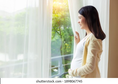 Happy pregnant mother wake up in morning and looking through window for seeing nice view with smile face and happiness at home Attractive single mom stay alone at house Young mom get relax Copy space