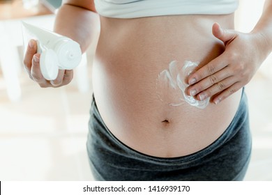 Happy pregnant woman apply skincare cream lotion on pregnant belly to prevent stretch mark. Healthy skin massage treatment and moisture care concept.