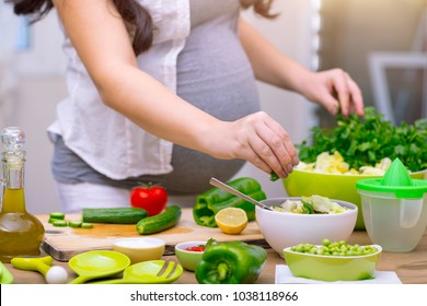 Mulher grávida feliz cozinhar em casa, fazer salada verde fresca, comer muitos vegetais diferentes durante a gravidez, conceito de gravidez saudável
