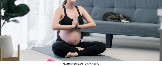 Happy pregnant woman during lotus posing practice sitting meditating yoga in the living room, to keep her prenatal healthy. Concept healthy pregnancy. Use for banner cover. - Shutterstock ID 2209211827