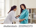 Happy pregnant woman has appointment with doctor at clinic. Female gynaecologist OB GYN medic specialist with stethoscope listens to baby