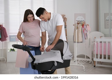 Happy Pregnant Woman With Her Husband Choosing Baby Stroller In Store. Shopping Concept