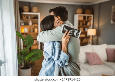 Happy pregnant woman with hug her husband and watch ultrasound photo of baby - Powered by Shutterstock