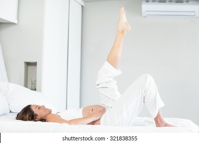 Happy Pregnant Woman With Leg Up While Lying On Bed