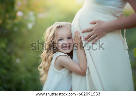 Happy pregnant woman with little daughter in a green tea rose garden