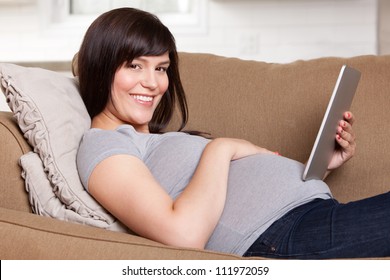 Happy pregnant woman looking at camera, using a digital tablet - Powered by Shutterstock