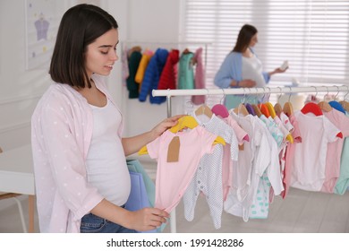 Happy Pregnant Woman With Shopping Bags Choosing Baby Clothes In Store