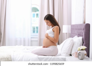 Happy Pregnant Woman Sitting On Bed At Home