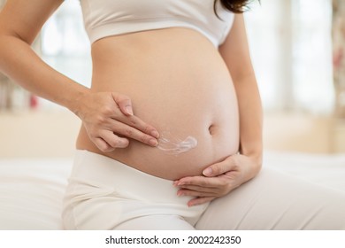 Happy Pregnant Woman sitting on bed holding and stroking apply cream on big belly for beauty moisturizing skin at home,Pregnancy young woman enjoying with belly soft skin,Beauty Pregnant Concept - Powered by Shutterstock