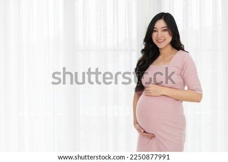 happy pregnant woman stroking her belly on window background