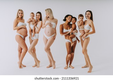 Happy pregnant women with big belly and beautiful mothers with babies in studio - Multiracial group of pregnant women and moms with children wearing underwear 