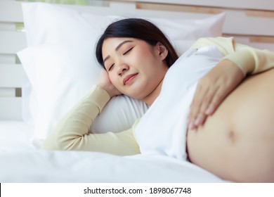 Happy Pregnant Young Asian Woman Touching Abdomen And Laying Down On Bed With Sleep Well And Smile Face. Young Asia Single Mother Love Her Baby So Much. Mom Waiting And Expecting Baby Has Good Health