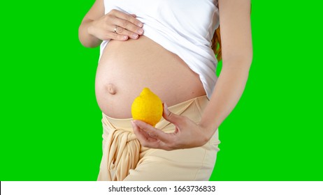 A Happy Pregnant Young Woman Holding A Lemon Next To Her Belly Showing The Size Of The Baby Inside Her Belly. Photos Of Fetal Growth At 14 Weeks Pregnancy. Healthy Pregnancy Diet With Vitamin C.