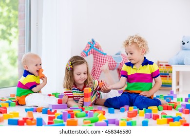 Happy preschool age children play with colorful plastic toy blocks. Creative kindergarten kids build a block tower. Educational toys for toddler or baby. Siblings having fun playing together.