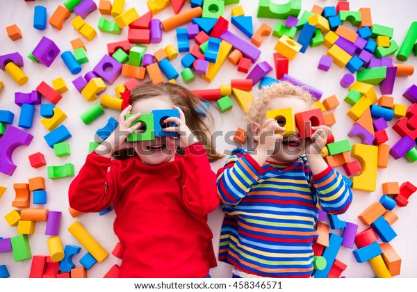 Happy preschool\
age children play with colorful plastic toy blocks. Creative\
kindergarten kids build a block tower. Educational toys for toddler\
or baby. Top view from\
above.