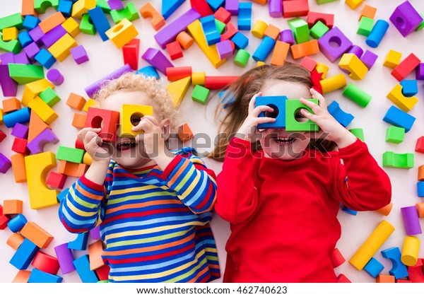 Happy preschool\
age children play with colorful plastic toy blocks. Creative\
kindergarten kids build a block tower. Educational toys for toddler\
or baby. Top view from\
above.