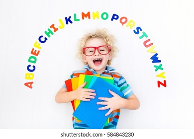 Happy Preschool Child Learning To Read And Write Playing With Colorful Roman Alphabet Letters. Educational Abc Toys And Books For Kids. School Student Doing Homework. Kid Reading In Kindergarten.