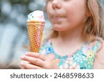 Happy preschool girl eating colorful ice cream in waffle cone on sunny summer day. Little toddler child eat icecream dessert. Sweet food on hot warm summertime days. Bright light, colorful ice-cream