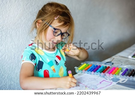 Happy preschool girl with glasses learning painting with colorful pencils and felt pens. Little toddler drawing at home on sunny summer day, using colorful feltpens. Creative activity for children.