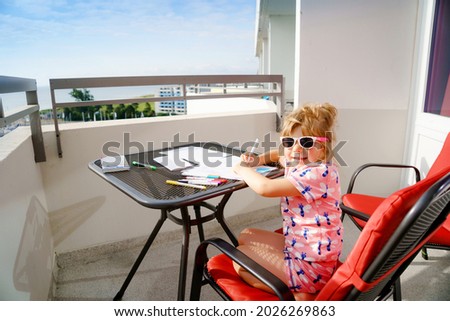 Happy preschool girl learning painting with colorful pencils and felt pens. Little toddler drawing at home on balcony on sunny summer day, using colorful feltpens. Creative activity for children.