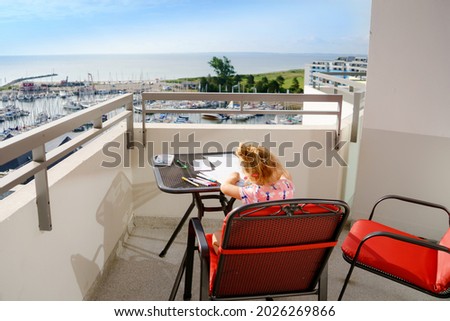 Happy preschool girl learning painting with colorful pencils and felt pens. Little toddler drawing at home on balcony on sunny summer day, using colorful feltpens. Creative activity for children.