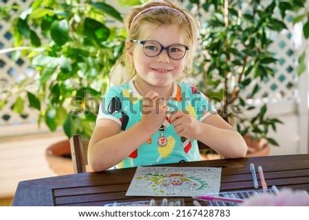 Happy preschool girl learning painting with colorful pencils and felt pens. Little toddler drawing at home on sunny summer day, using colorful feltpens. Creative activity for children.